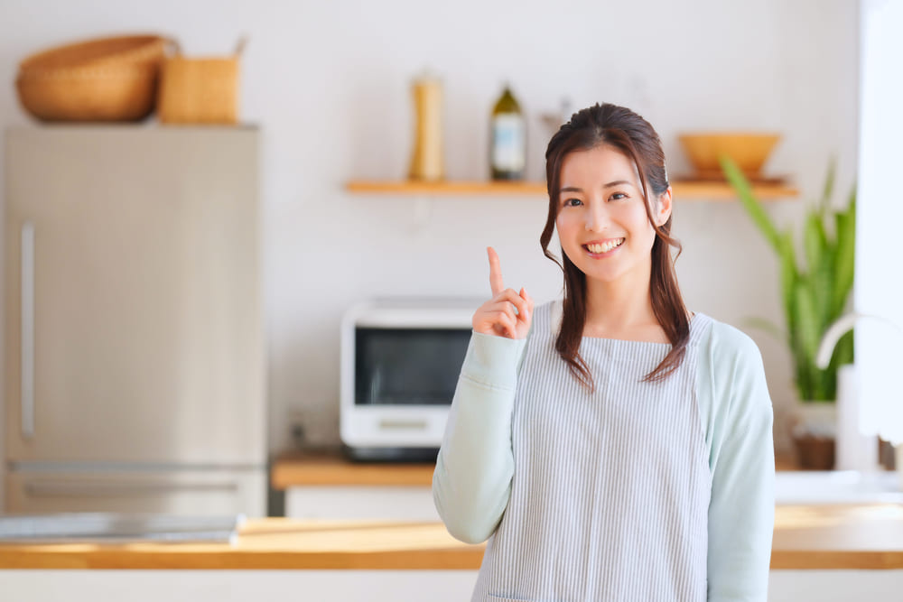 キッチンの前で笑顔で指を一本立てる女性